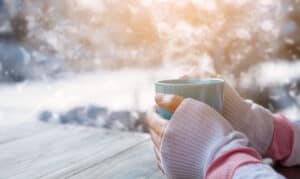 vrouw die haar koude handen opwarmt aan een kop warme thee
